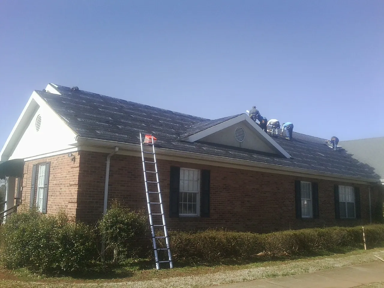 Crew tearing shingles off a brick ranch roof with a ladder set — Metal Roof Repair work by our crew in Glens Falls