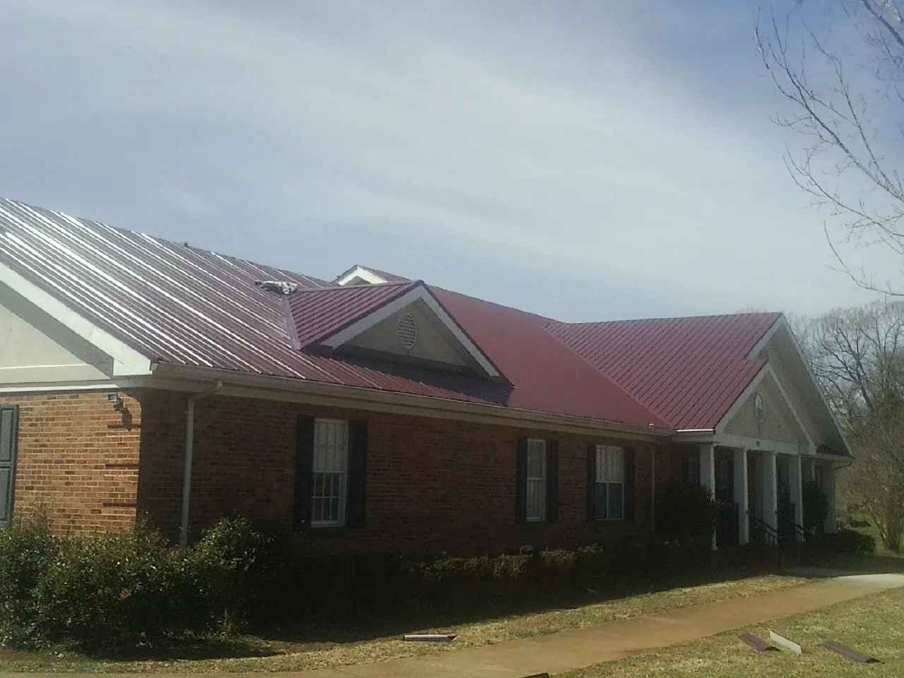 Red metal roof with gabled entries on a long brick building, from a Hail Damage Roof Repair job in Glens Falls