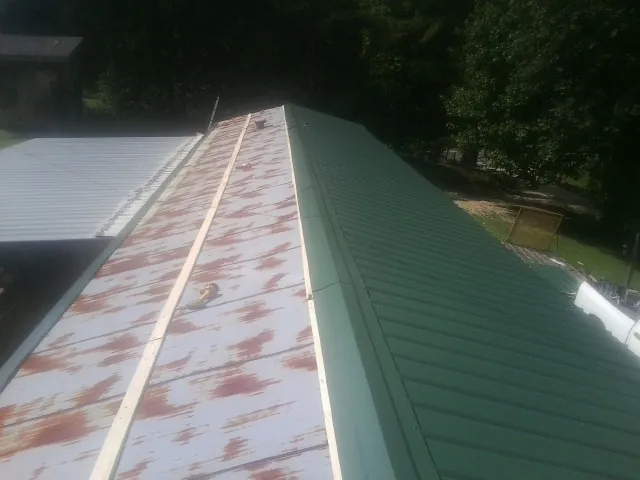 Old rusted panels beside newly installed green metal roofing — Wind Damage Roof Repair by Roofing Brothers in Glens Falls