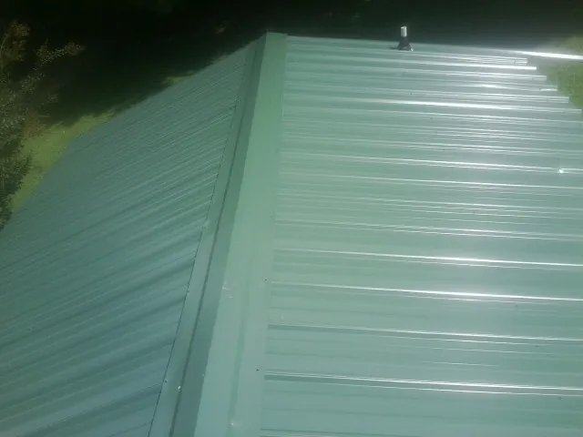 New green metal panels meeting at the ridge of a roof — Flat Roof Repair work by our crew in Glens Falls