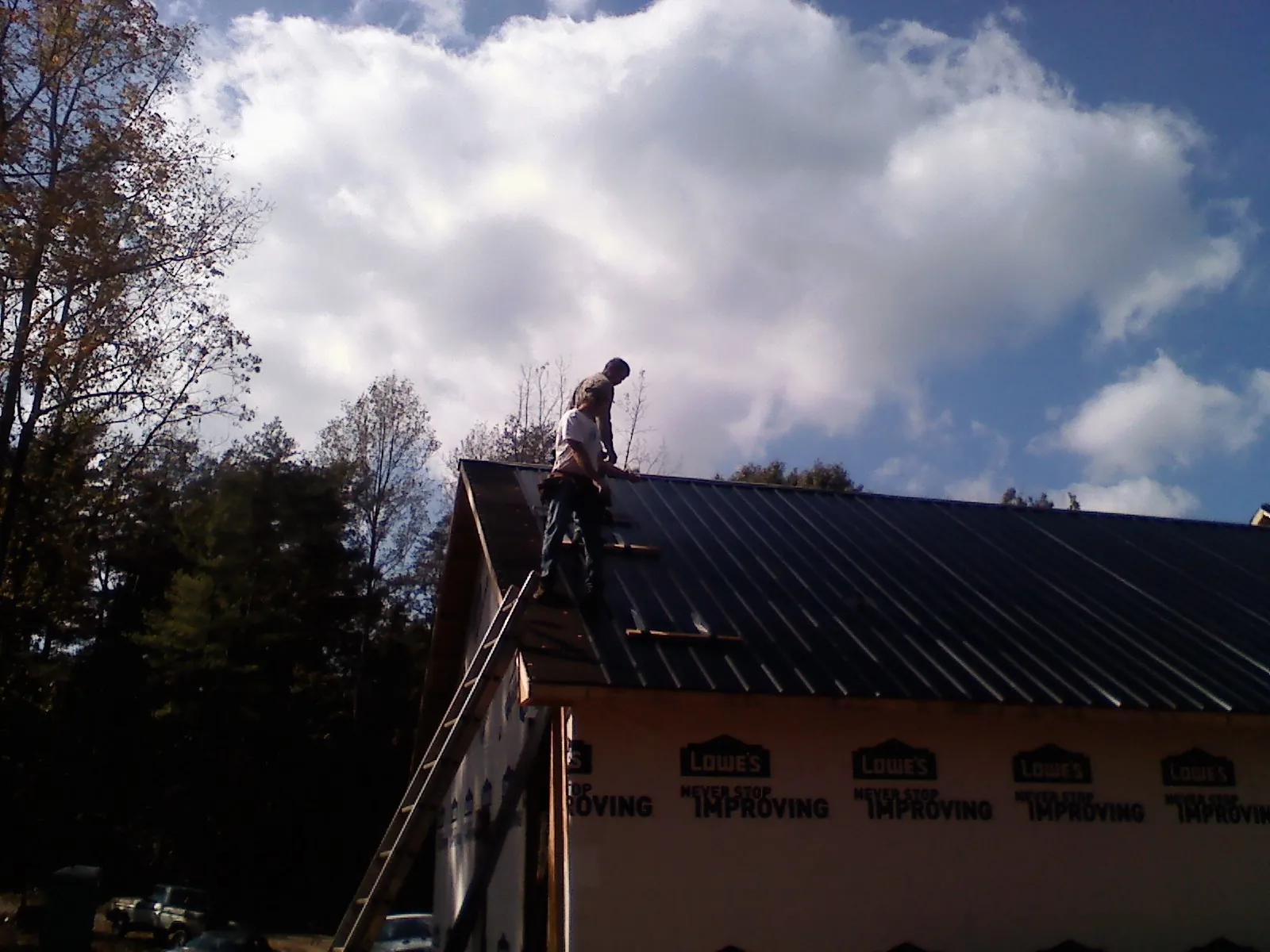 Roofer fastening dark metal panels high against a cloudy sky, from a Roof Inspection job in Glens Falls