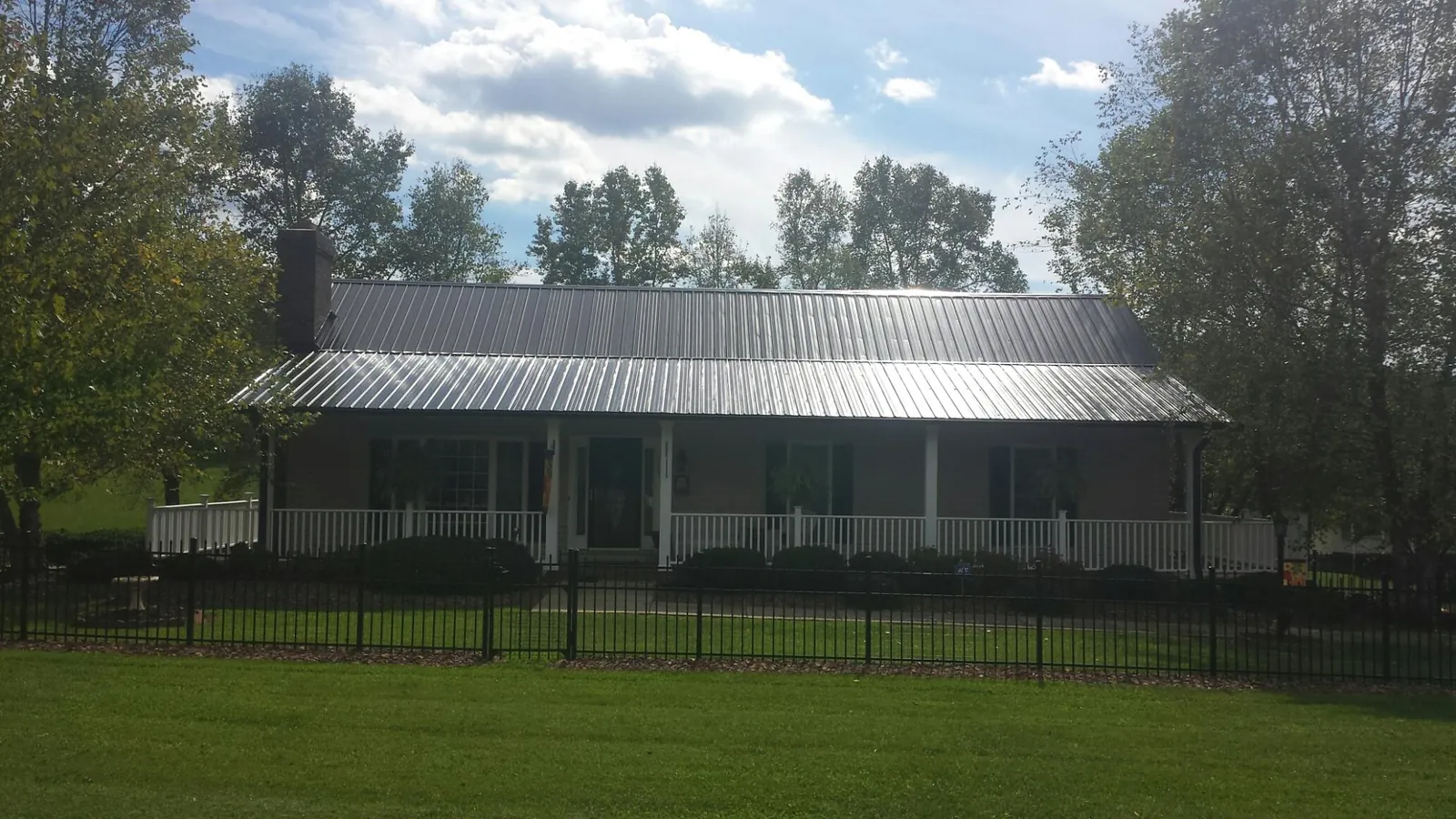 Gray metal roof on a brick ranch with a full width front porch — Gutter Guard Installation work by our crew in Glens Falls