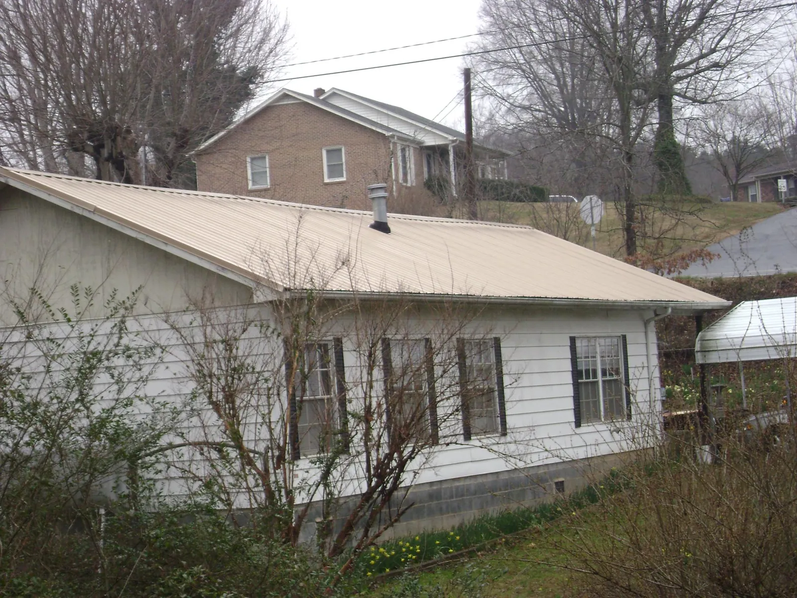 Tan metal roof on a white sided house set into a hillside — Commercial Roofing by Roofing Brothers in Glens Falls