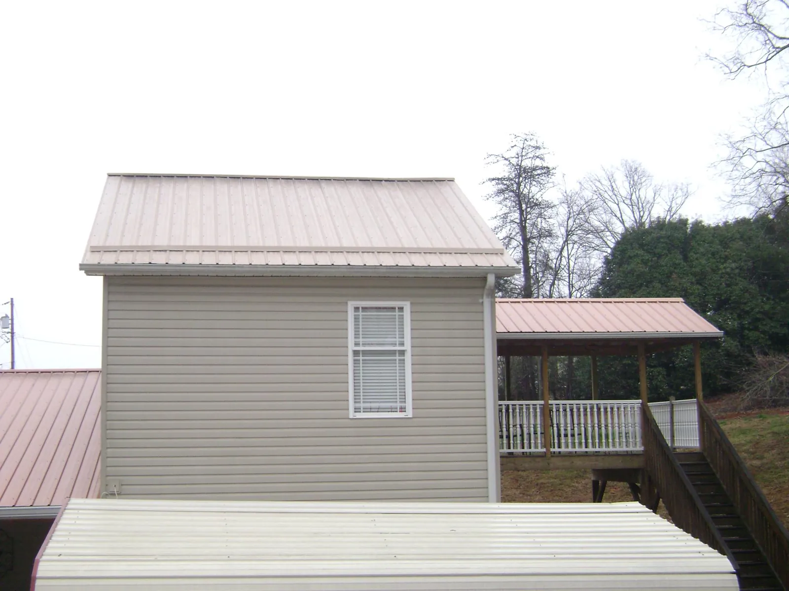 Tan metal roofs on a two story addition and attached porch, from a Roof Replacement job in Glens Falls